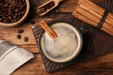 Cup of hot coffee with aromatic cinnamon on wooden table, flat lay