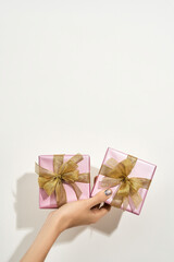 Happy Womens day. Vertical shot of a female hand holding two small wrapped gift boxes with golden bows against white background