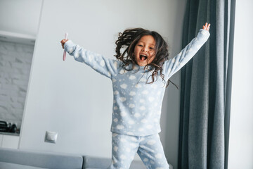 Happy young little girl have fun by jumping on the bed at home