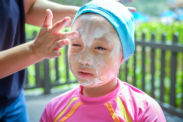 mom applying sunscreen on girl face before swim.