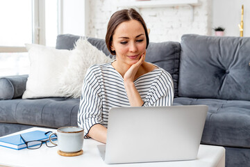 Portrait of young woman using laptop at home.