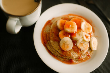 gluten free homemade pancake with strawberry marmalade and sliced banana closeup photo with hot coffee and dark background