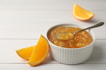 Fototapeta na wymiar Delicious orange marmalade in bowl with spoon on white wooden table, space for text