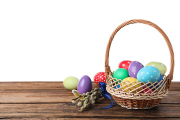 Colorful Easter eggs in wicker basket and willow branches on wooden table against white background. Space for text