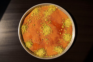 Eastern dessert kunafa in a big aluminium dish on dark black background. Top view. Arabic cheese kunafa on dark. Konafa.