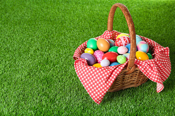 Wicker basket with Easter eggs on green grass. Space for text