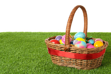 Wicker basket with Easter eggs on green grass against white background. Space for text