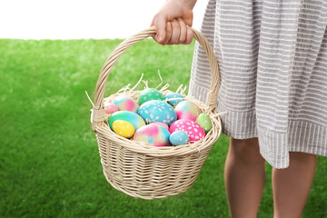 Little girl with basket full of Easter eggs on green grass against white background, closeup