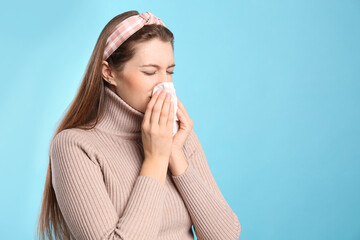 Young woman with tissue suffering from runny nose on light blue background. Space for text