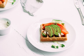 Belgian waffles with salmon, avocado and cream cheese on a white plate. Healthy breakfast