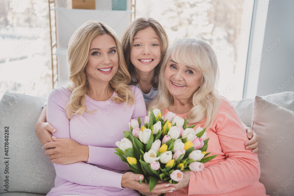 Poster Photo portrait of grandmother daughter granddaughter spending time together embracing on sofa keeping tulips bunch