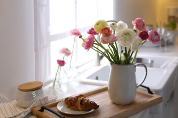 Wooden tray with beautiful ranunculus flowers and fresh croissant in kitchen