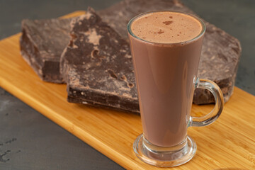 Hot cocoa drink in glass cup and chocolate bar on gray background