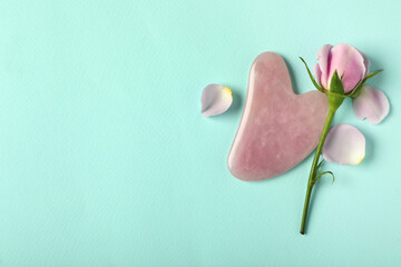 Rose quartz gua sha tool and flower on light blue background, flat lay. Space for text