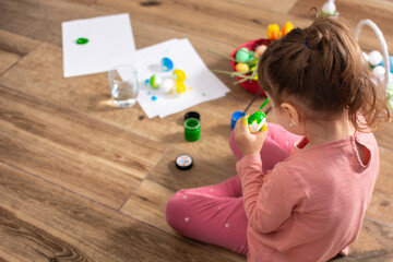 Baby girl painting Easter eggs at home