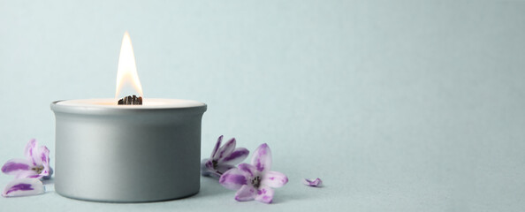 Beautiful candle with wooden wick and flowers on light background, space for text