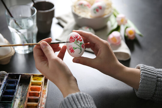 Woman painting Easter egg at black table, closeup