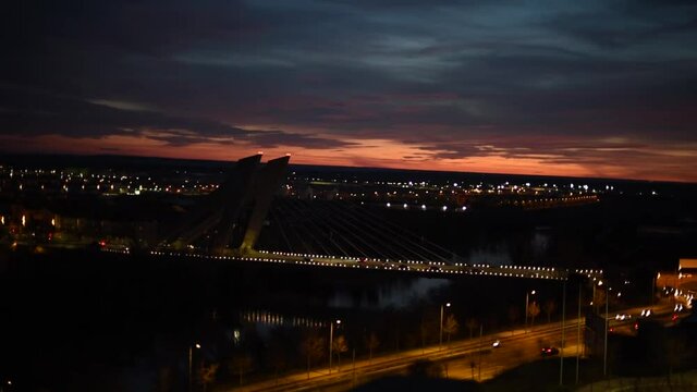 Paisaje urbano nocturno con puente y puesta de sol visto desde la cima de un monte. Desenfoque y bokeh de las luces de la ciudad de noche. Puente de la Hispanidad en Valladolid, Espa&ntilde;a.