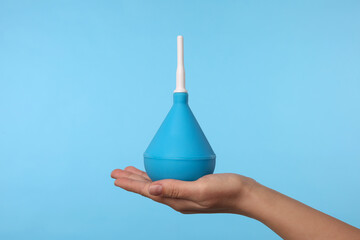Woman holding enema on light blue background, closeup