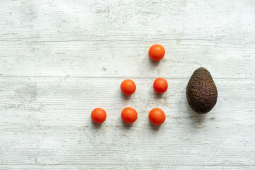 avocado and fresh cherry tomatoes on white wooden background with conceptual shapes