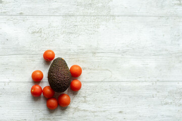 avocado and fresh cherry tomatoes on white wooden background with conceptual shapes