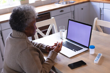 African american senior woman holding empty medication container while having a videocall on laptop