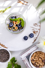 Fototapeta na wymiar Chia pudding with granola, blueberries, hazelnut on white wooden stand. Top view