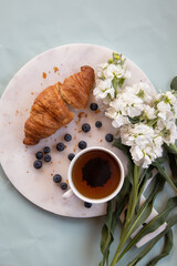 A marble plate with a cup with tea and croissant and blueberries on it with white flowers