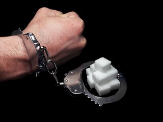 Handcuffed man is addicted to sugar and cocaine, sugar is more addictive than cocaine, white sugar cube and cocaine drug powder pile are linked with handcuffed addicted man hand