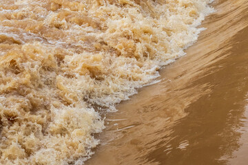 The brown turbid water rushed over the dam overflowing.