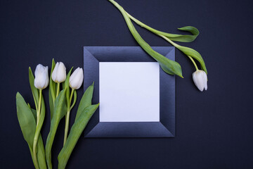 on a black background, lies a black frame with a white background and white tulips on the sides