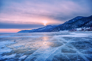Cracks on the surface of blue ice. Frozen lake in the winter mountains. Sunset