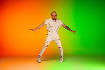 Fototapeta na wymiar Urban. Stylish sportive caucasian man dancing hip-hop on colorful gradient background at dance hall in neon light. Youth culture, movement, style and fashion, action. Fashionable bright portrait.