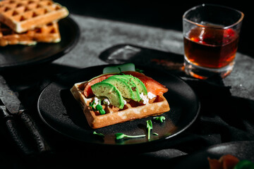 Belgian waffles with salmon, avocado and cream cheese on a black plate. Healthy breakfast
