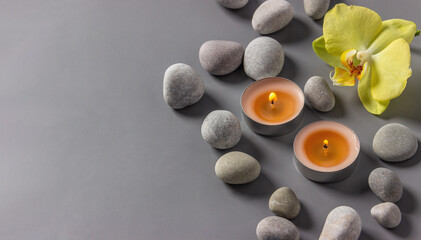 Aromatic  candles, orchid flower and stones on a gray background.  Spa composition. Relaxation and zen like concept..