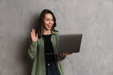 Happy beautiful girl waving hand while using laptop