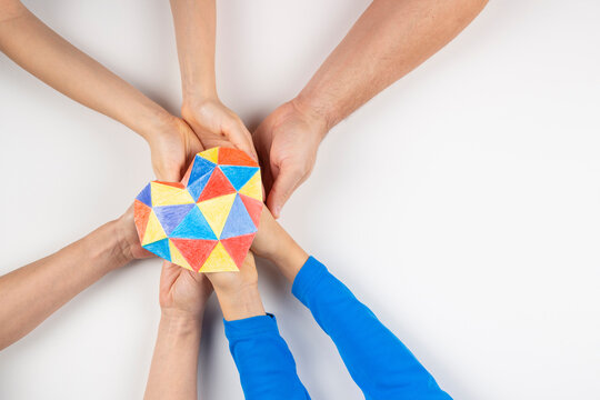 Family hands holding colorful paper heart on white background. Autism spectrum disorder family support. World autism awareness day concept