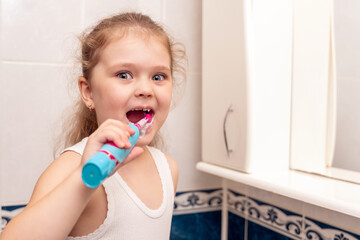 Little girl brushes her teeth with an electric toothbrush in the morning in the bathroom