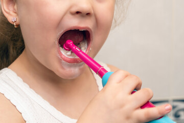 Little girl brushes her teeth with an electric toothbrush in the morning in the bathroom