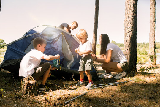 camping tourism, family and people concept - happy parents and son setting up tent hike outdoors