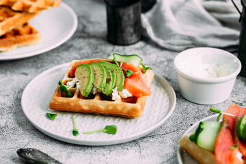 Belgian waffles with salmon, avocado and cream cheese on a white plate. Healthy breakfast at the table