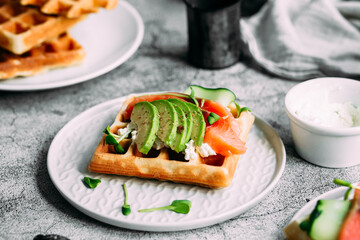 Belgian waffles with salmon, avocado and cream cheese on a white plate. Healthy breakfast at the table