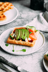 Fototapeta na wymiar Belgian waffles with salmon, avocado and cream cheese on a white plate. Healthy breakfast at the table