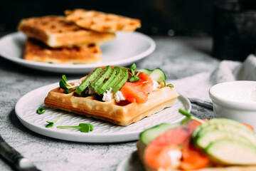 Belgian waffles with salmon, avocado and cream cheese on a white plate. Healthy breakfast at the table
