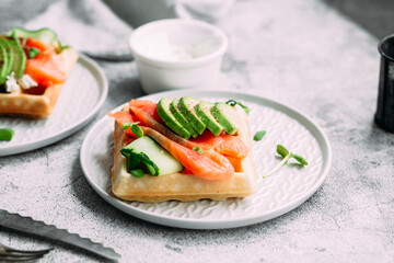 Belgian waffles with salmon, avocado and cream cheese on a white plate. Healthy breakfast at the table