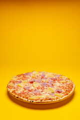 Vertical frame of simple Hawai pineapple ham oven pizza with crunchy crest and golden yellow orange tint. Studio food still life against a seamless yellow background