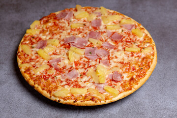 Modern kitchen gray surface with simple Hawai pineapple ham oven pizza with crunchy crest and golden yellow orange tint. Studio food still life against a seamless yellow background