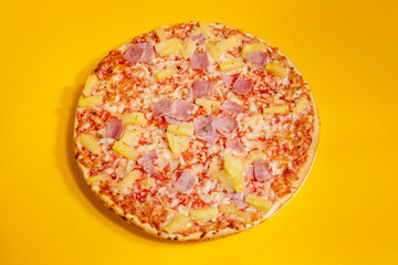 Top down view of simple Hawai pineapple ham oven pizza with crunchy crest and golden yellow orange tint. Studio food still life against a seamless yellow background