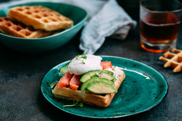 Belgian waffles with salmon, poached egg, avocado and cream cheese on a turquoise plate. Healthy breakfast at the table