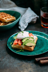 Belgian waffles with salmon, poached egg, avocado and cream cheese on a turquoise plate. Healthy breakfast at the table